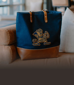 Navy Notre Dame Tote with Leppy the leprechaun logo on a leather sofa