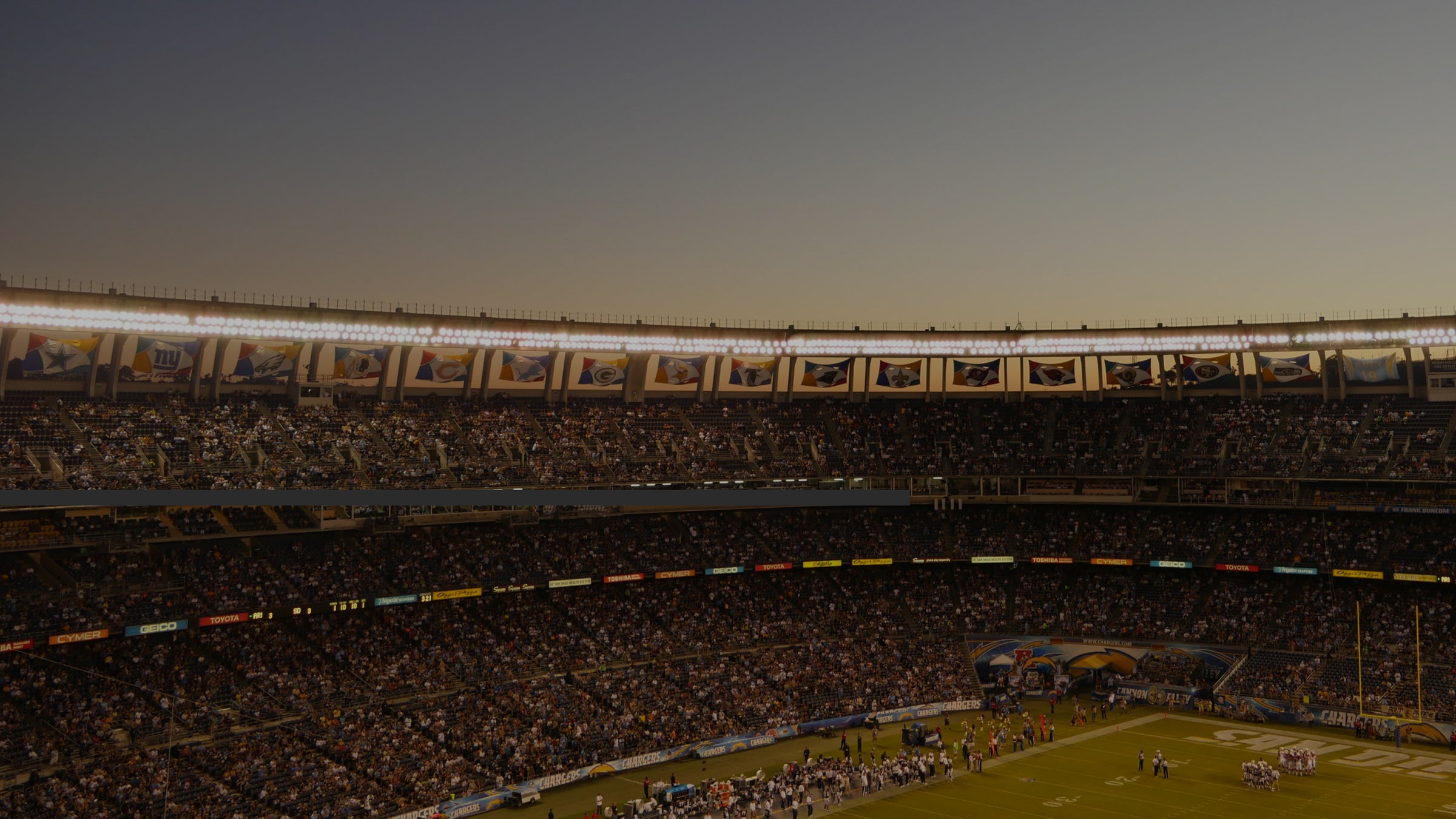 inside a busy, outdoor football stadium, lit up at dusk